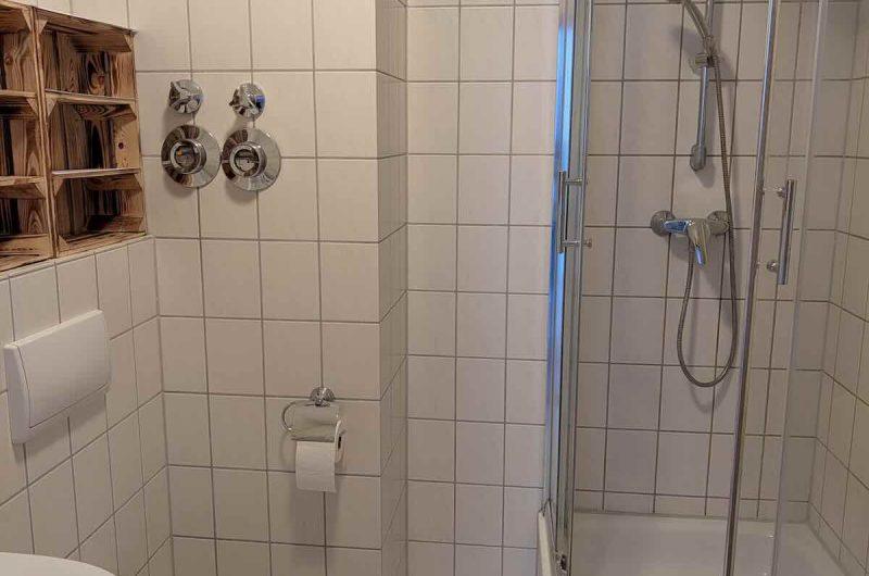 Gepflegtes, raumhoch weiß gefliestes Badezimmer mit Glas-Duschkabine und praktischen Ablagemöglichkeiten.