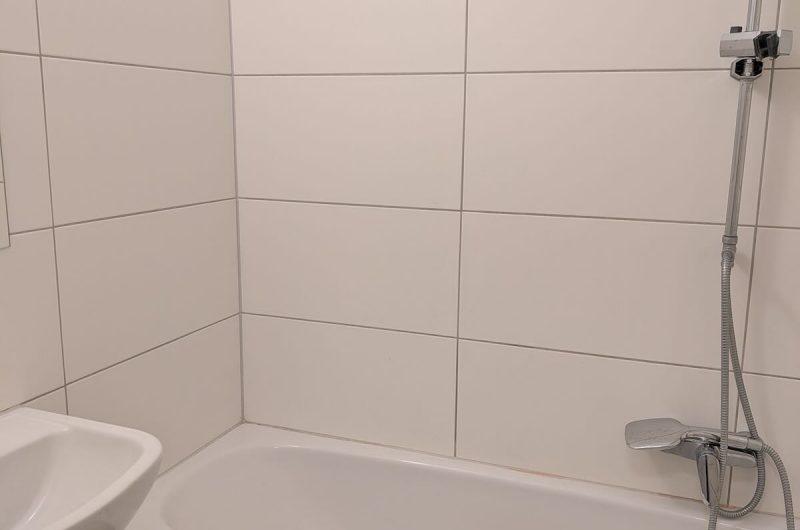 Gepflegtes, hell gefliestes Badezimmer mit Badewanne und Duschmöglichkeit.