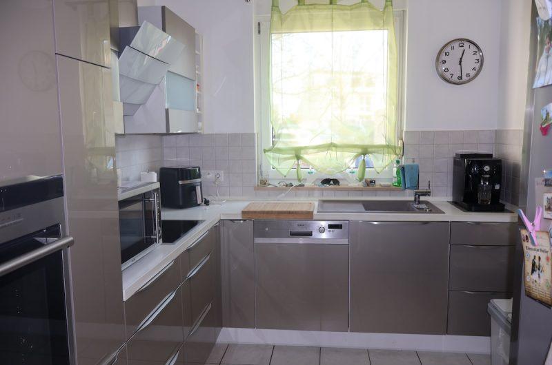 Moderne Einbauküche in L-Form mit hochwertigen Elektrogeräten, hellen Fronten und Fenster zum Vorgarten.