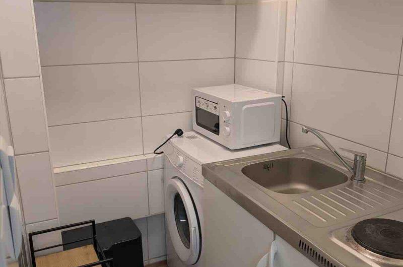 Kompakte Einbauküche mit Waschmaschine und hellen Schränken in der Mietwohnung.