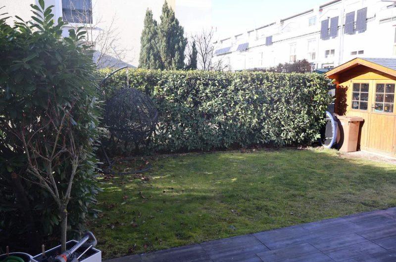 Blick in den blickgeschützten Garten mit grüner Hecke, Rasenfläche und gemütlichem Hängesessel im Pinderpark.