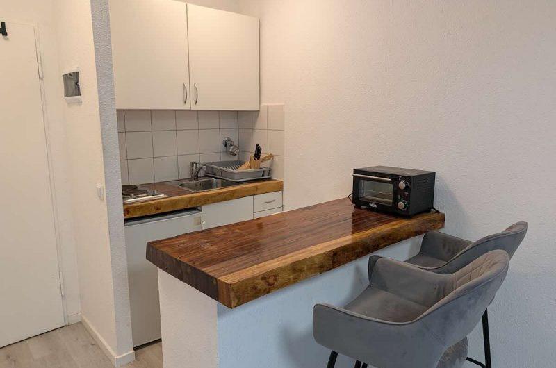 Kompakte Küchenzeile mit hellen Fronten und bereits installierter Waschmaschine.