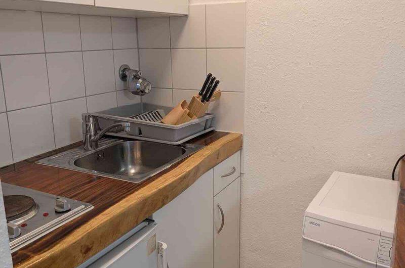 Kompakte Pantry-Küche in der 29m² Wohnung in Nürnberg mit Waschmaschine, Mikrowelle und Schränken in dekorativer Fliesen-Optik.