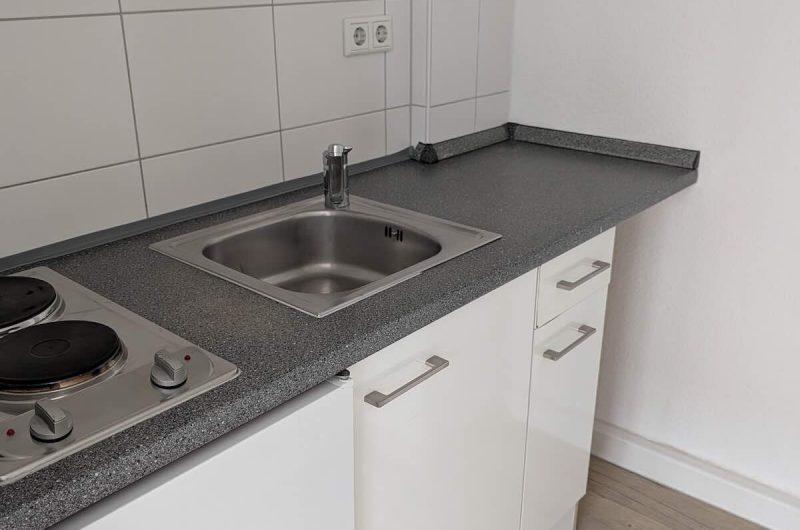 Kompakte weiße Einbauküche mit Kochfeld und Spüle im Apartment.