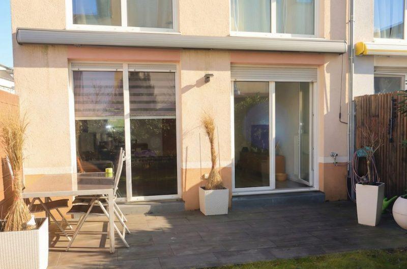 Einladende Süd-West-Terrasse mit neuer Markise, modernen Bodenplatten und Zugang zum Wohnzimmer eines Reihenhauses.