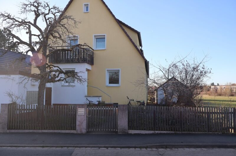 Fassadenansicht der Erdgeschosswohnung mit eingezäuntem Vorgarten und Terrasse.