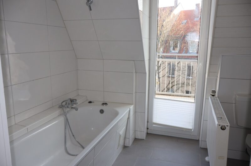 Weiße Badewanne im gefliesten Badezimmer mit Blickrichtung zur Terrasse.