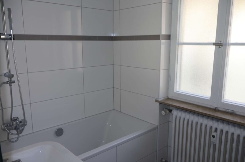 Neu saniertes Badezimmer mit hellen Fliesen, weißer Badewanne und Fenster in Nürnberg Sebald.