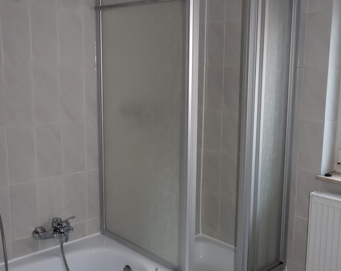 Badezimmer mit Dusche und Badewanne sowie hellen Fliesen.