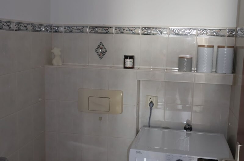Gepflegte Toilette mit Waschmaschinenanschluss und hellen Fliesen
