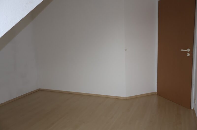 Leeres Schlafzimmer mit frisch verlegtem Laminat und weißen Wänden.