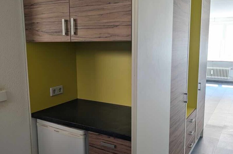 Hochwertige Einbauschränke in Holzoptik mit viel Stauraum und integriertem Kühlschrank im Eingangsbereich der Single-Wohnung.