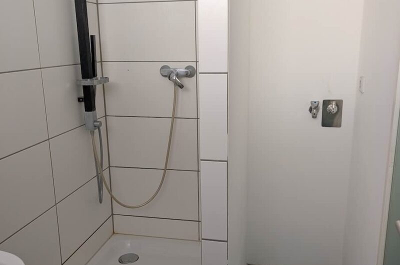 Geflieste Duschkabine mit moderner Duscharmatur und praktischem Waschmaschinenanschluss im sanierten Badezimmer von Maderer Immobilien.