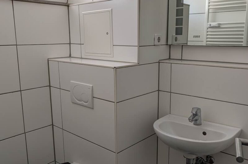 Modern saniertes Tageslichtbadezimmer mit weißen Fliesen, hängendem WC, Waschbecken und großem Spiegel in einer Nürnberger Single-Wohnung.