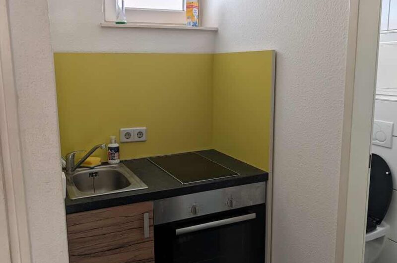 Kompakte, vollwertige Einbauküche mit Cerankochfeld, Backofen, hellem Fenster und modernen Farbakzenten in einer Single-Wohnung in Nürnberg.