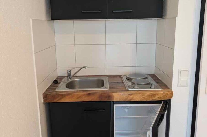 Ausgestattete Singleküche mit 2-Plattenherd, Spüle, Kühlschrank und Oberschrank in einem Nürnberger Apartment.