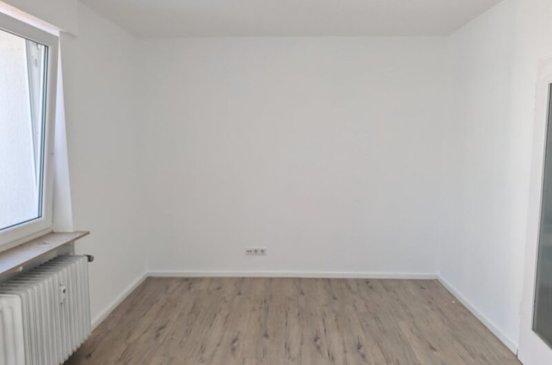 Blick durch das helle Zimmer auf das große Kunststofffenster und den modernen Bodenbelag.