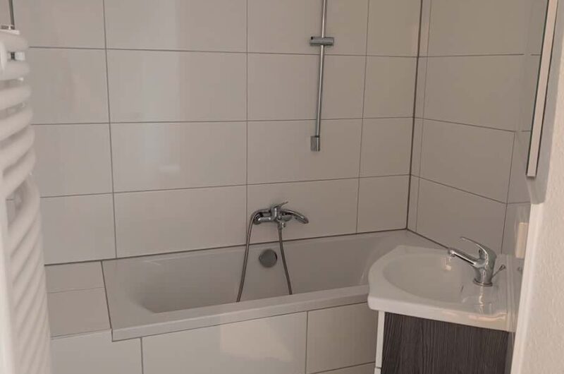 Weiß gefliestes Tageslichtbad mit Badewanne und Waschbeckenunterschrank