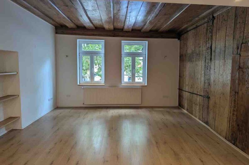 Helles Wohnzimmer mit originaler Holzbalkendecke und großen, modernen Fenstern im Nürnberger Zentrum.