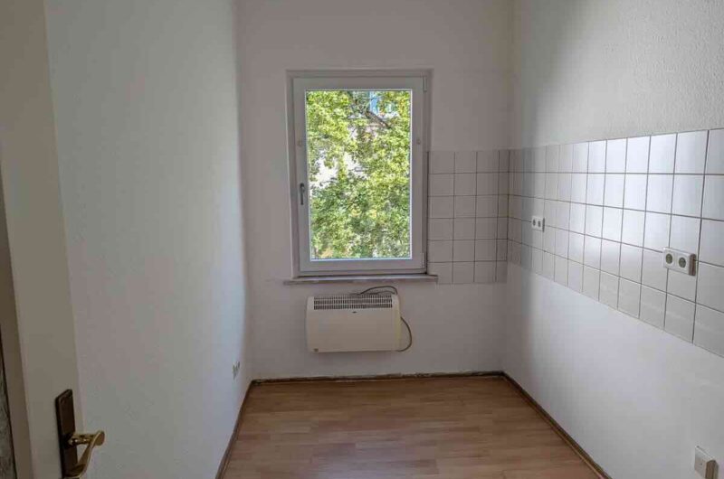 Heller Küchenraum mit großem Kunststofffenster, Laminatboden und weißem Fliesenspiegel.