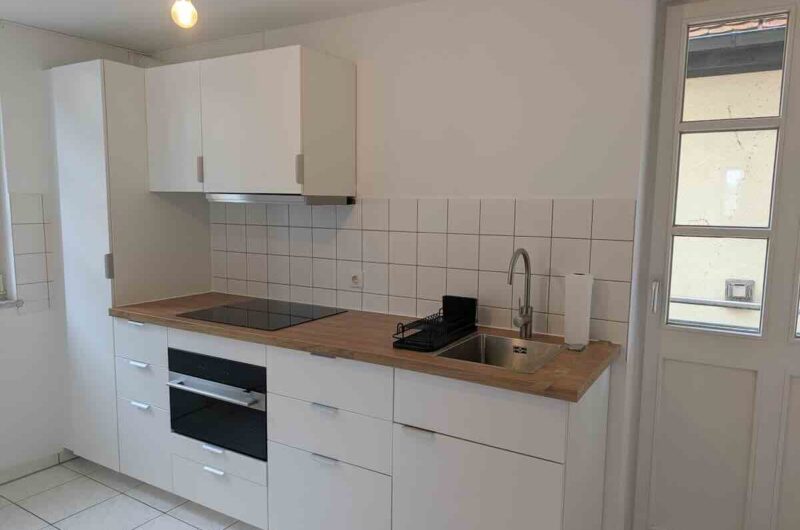 Moderne, weiße Einbauküche mit Holzarbeitsplatte und direkter Tür zum Balkon in Schwabach Zentrum – Maderer Immobilien.