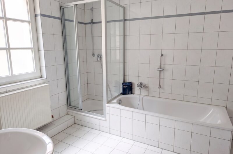Helles, weiß gefliestes Tageslichtbad mit Duschkabine und Badewanne in der Schwabacher Altstadt – ideal zur Entspannung nach der Radtour – Maderer Immobilien.
